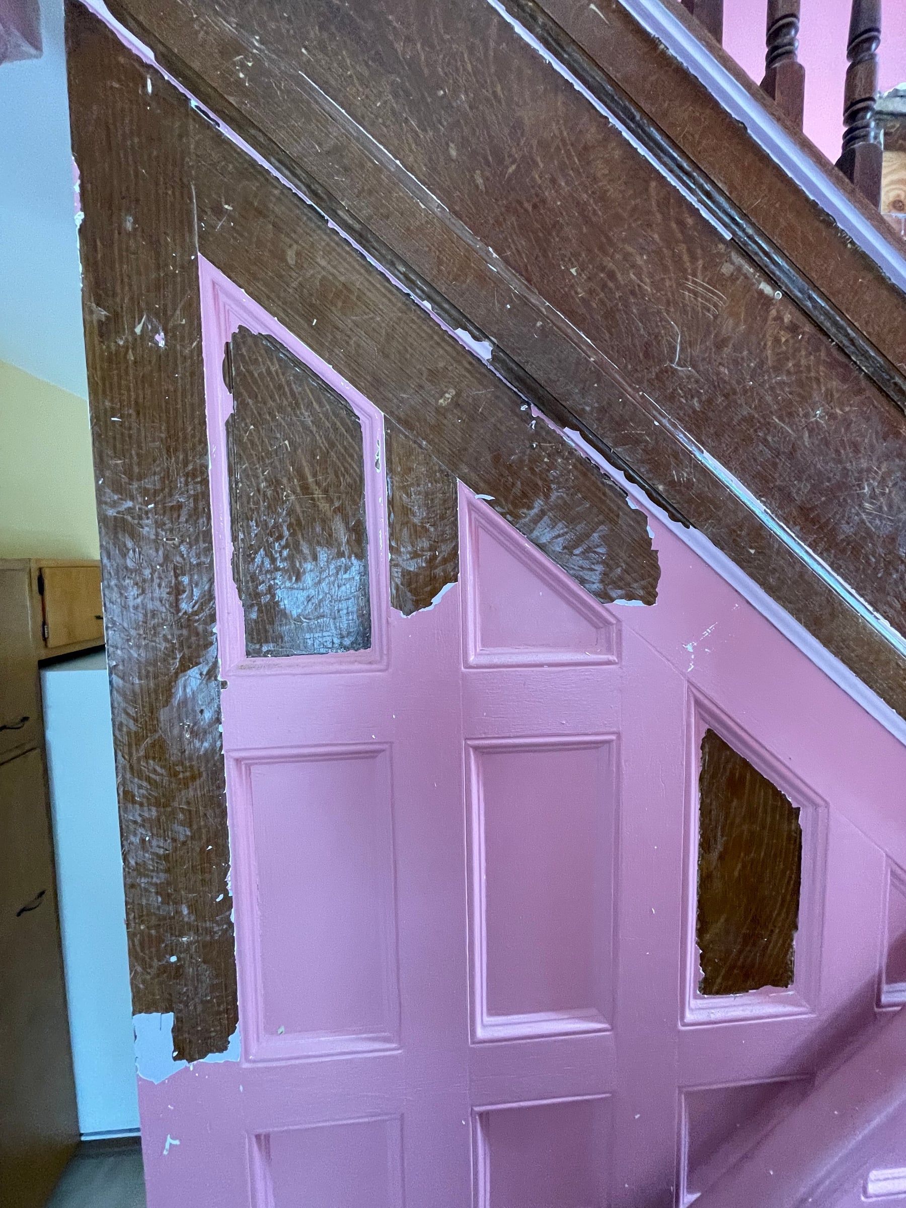 The side of the staircase with pink paint flaking away to show the original wood graining underneath
