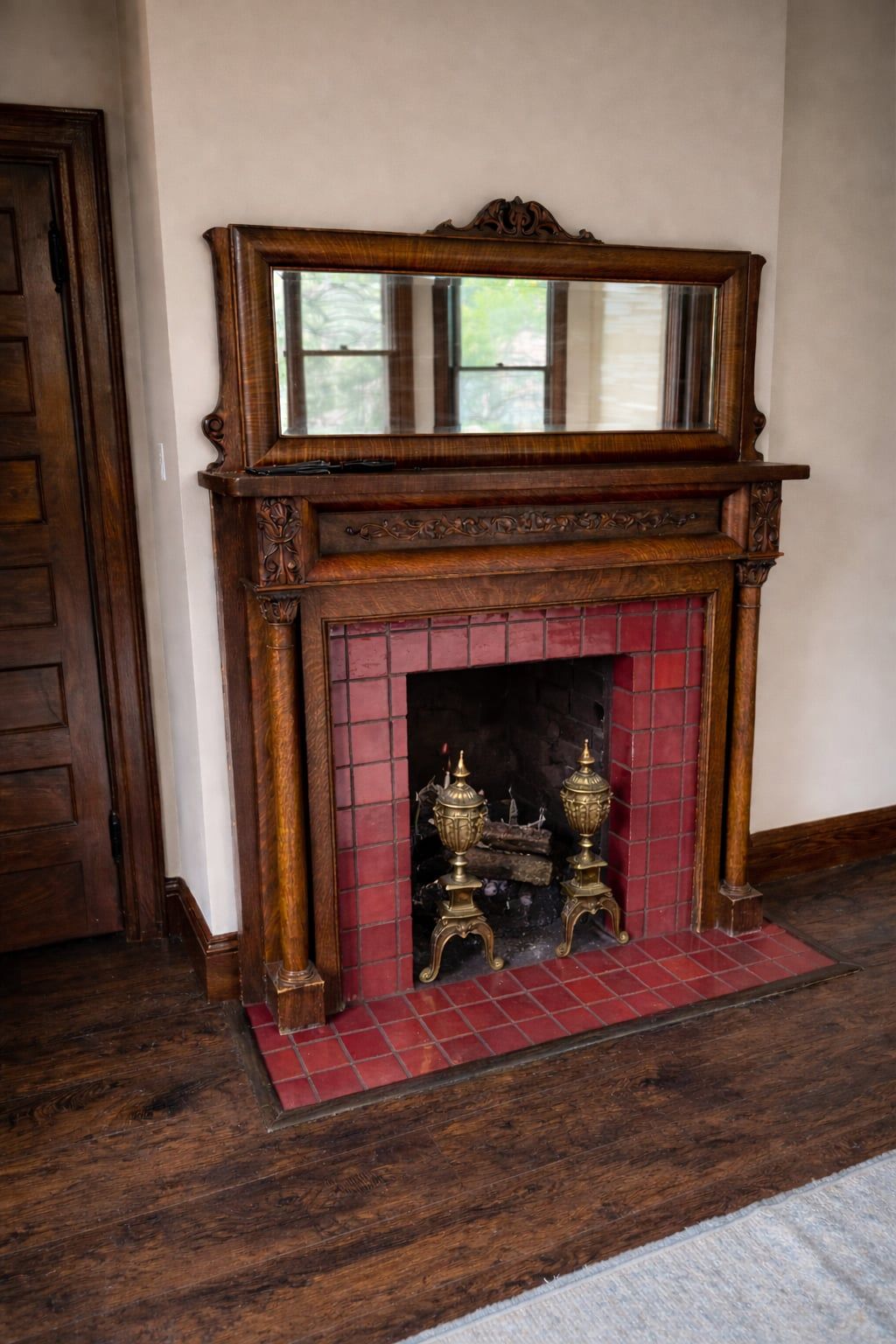 A carved oak mantel with a mirror above and a deep red tile surround, brass andirons in the firebox