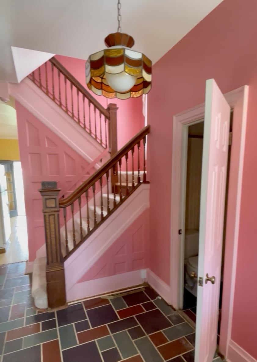 The front hall before: the same staircase and paneling painted pink, a slate tile floor, and a stained glass pendant light