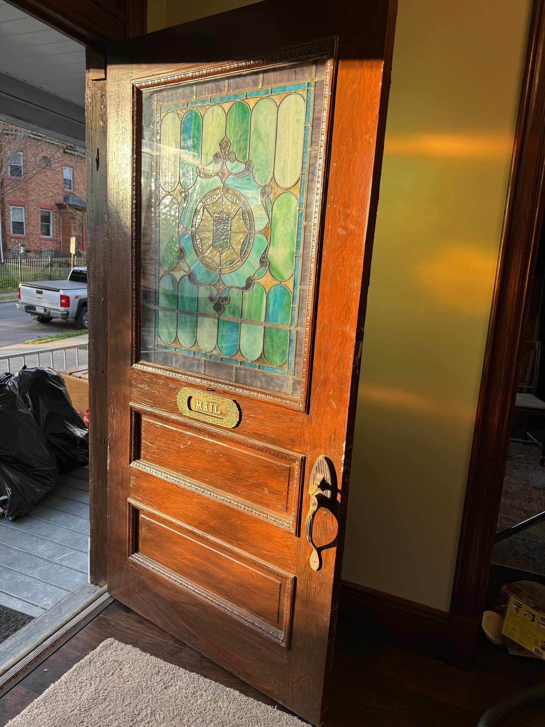 The front door open to the porch, its large stained glass panel lit by the low sun