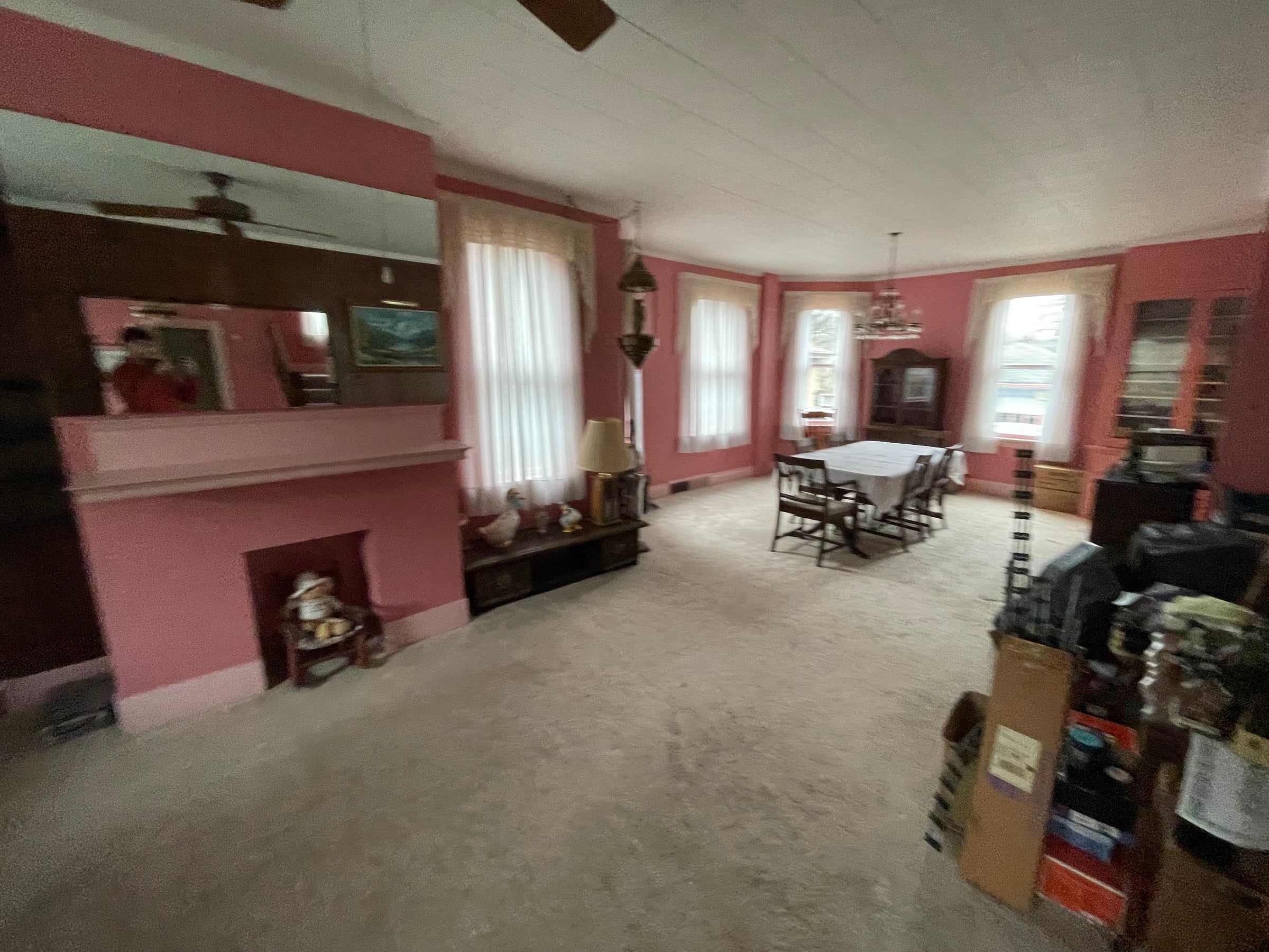 The living room before: pink walls, a pink painted fireplace with a mirror above, wall-to-wall carpet, and a tile drop ceiling