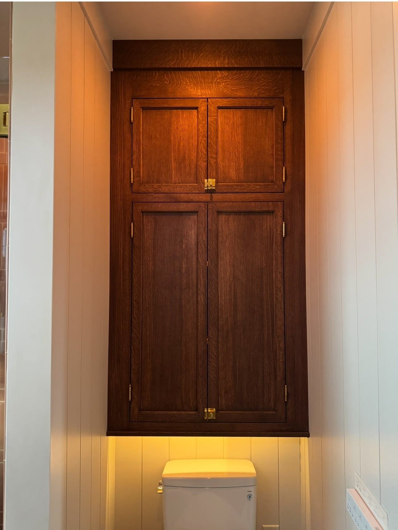 A tall quarter-sawn oak cabinet built into the wall above the toilet, its doors flush with the tank
