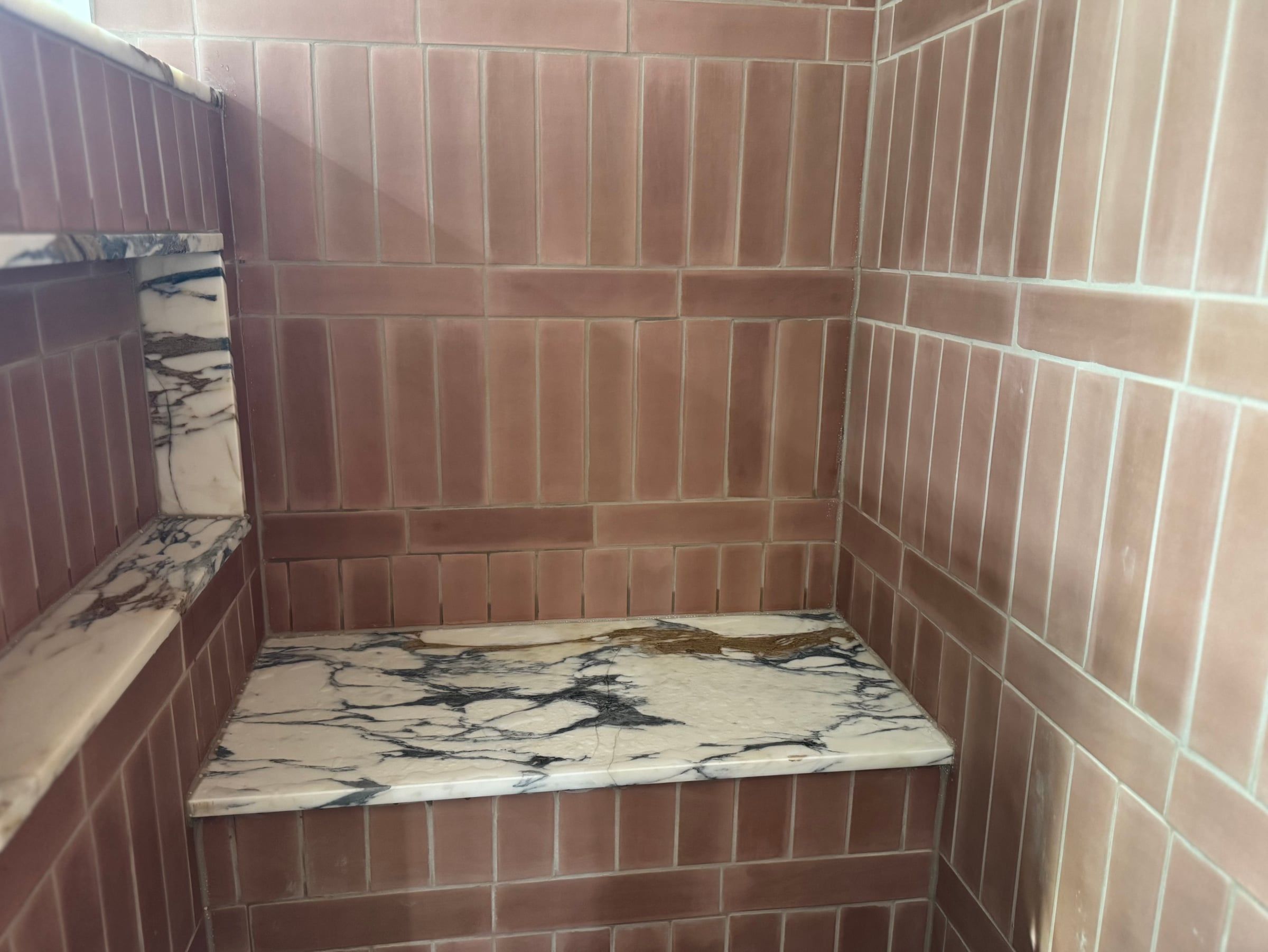 The shower bench and niche in white marble with dark veining, set into vertical terracotta-pink tile