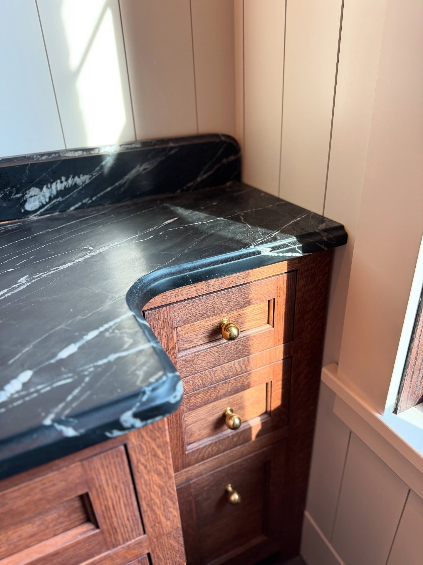 A corner of the vanity: inset quarter-sawn oak drawers with brass knobs under a black stone counter with white veining