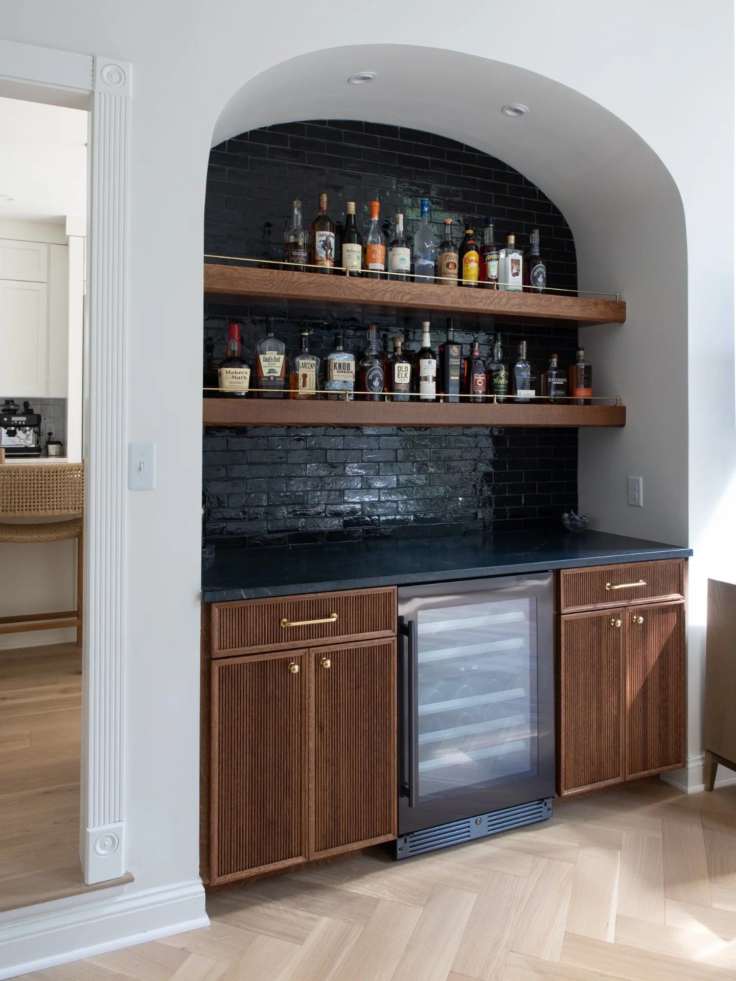 The bar in an arched nook: fluted quarter-sawn oak cabinets, floating oak shelves lit from beneath, and black handmade zellige tile