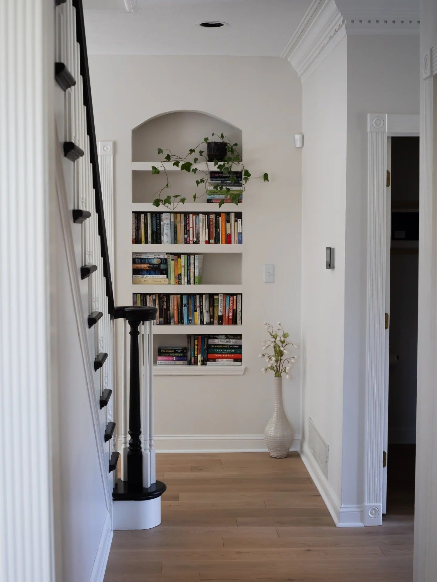 A small arched bookshelf built into a former nook at the foot of the stairs