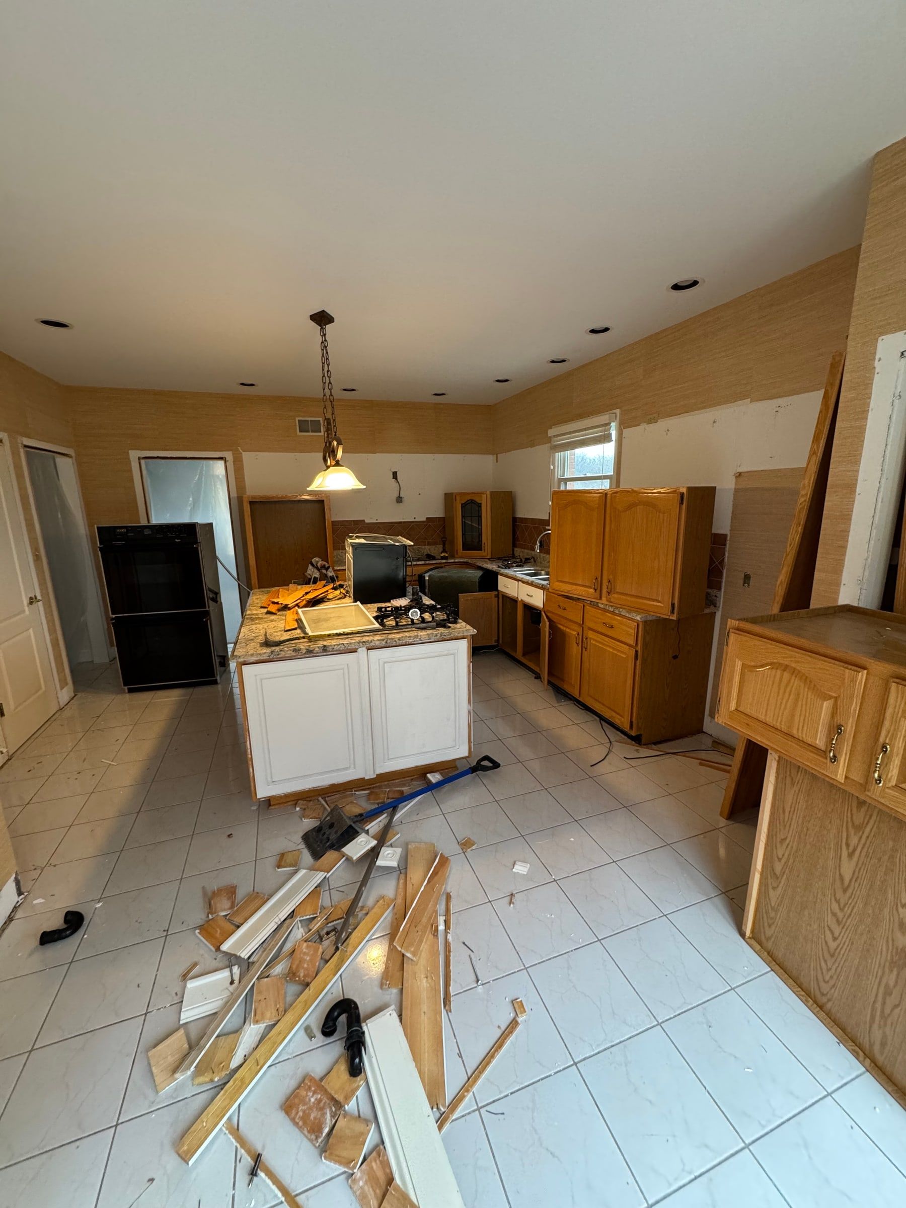 The kitchen before, mid-demolition: orange oak cabinets, a white tile floor, and the old island