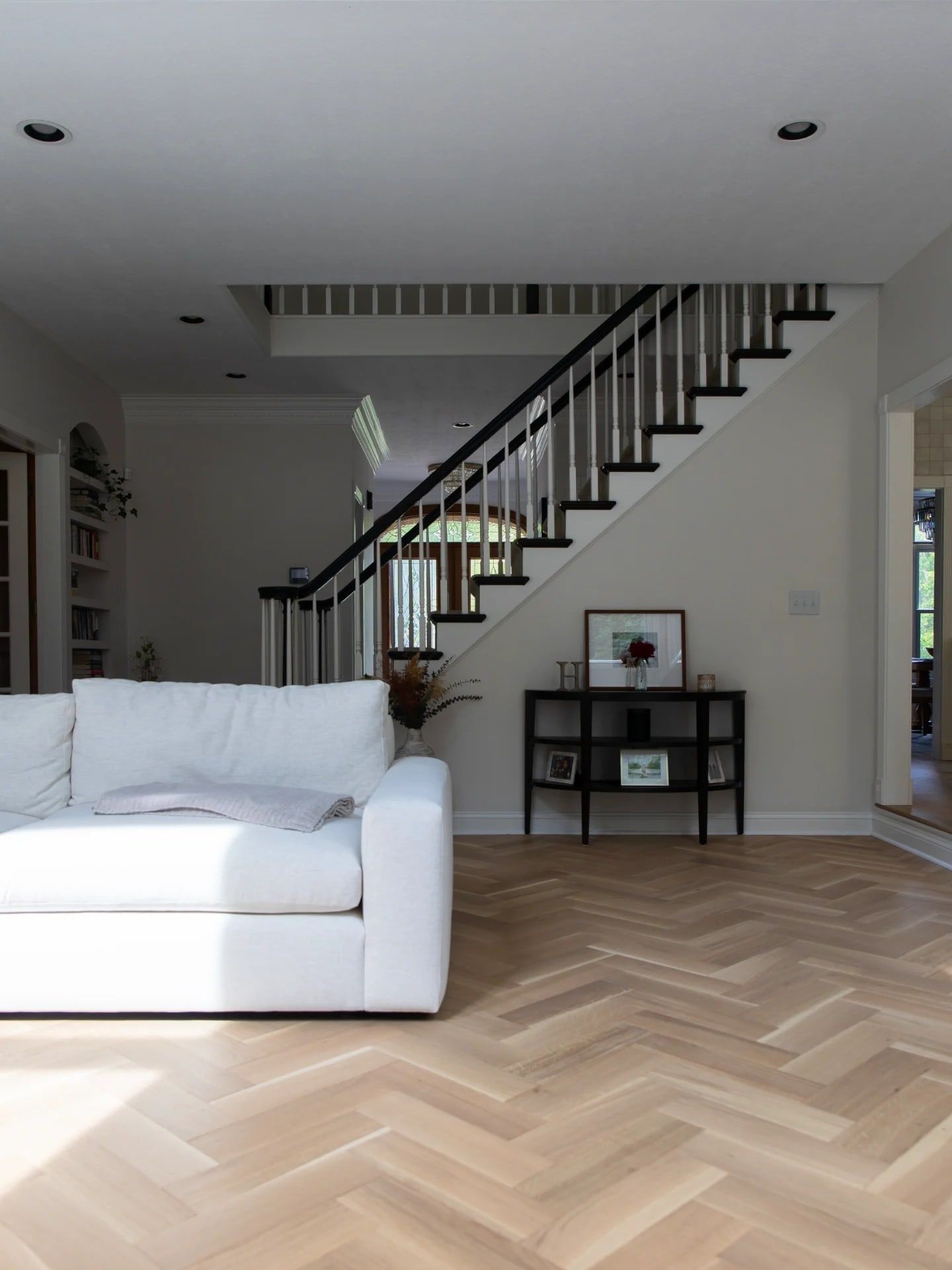 The living room’s white oak floor laid in herringbone, with the staircase beyond