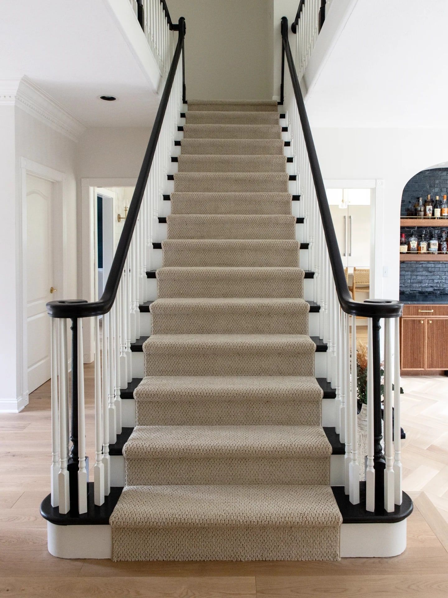 The full staircase from the front hall: ebony handrails, white spindles and risers, and a fresh runner