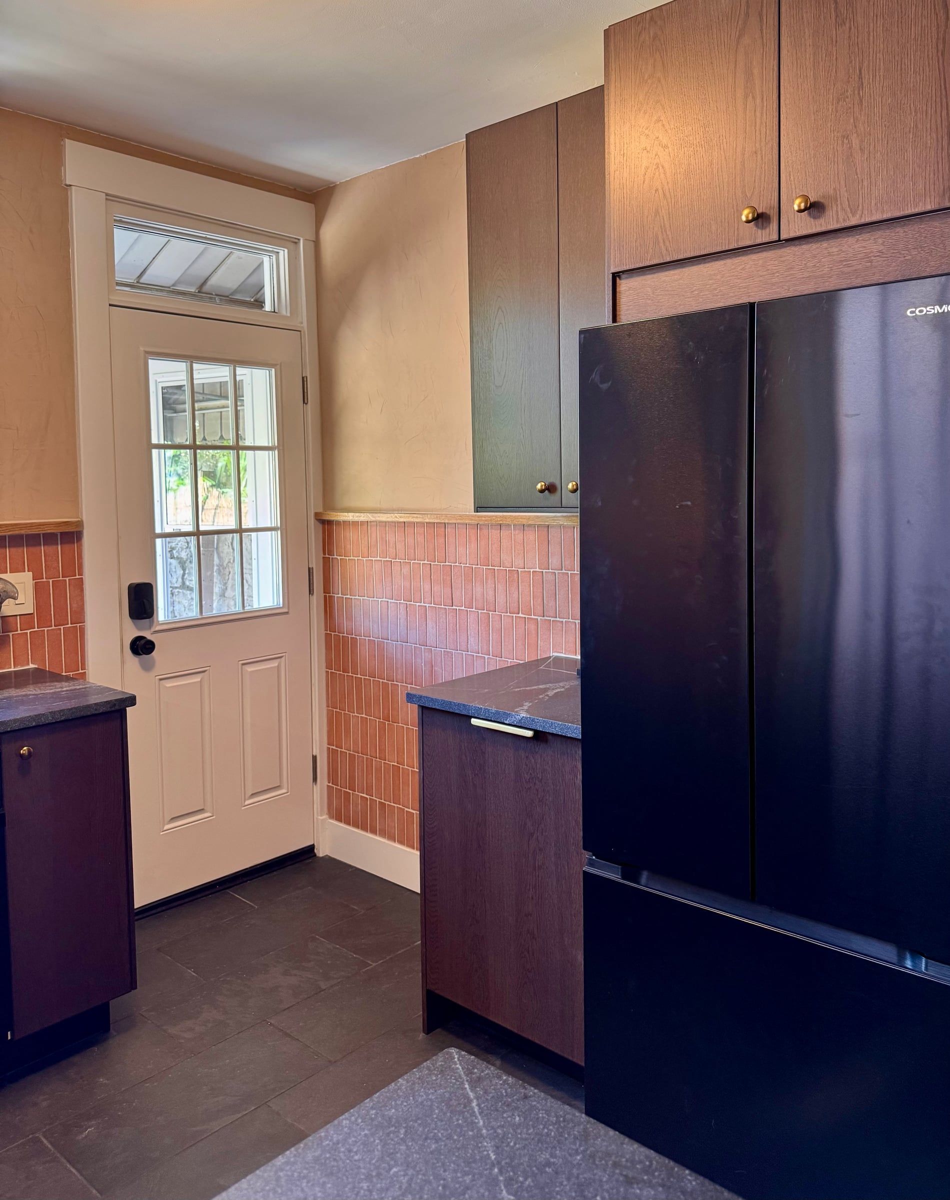 The back door corner: Roman clay walls above a terracotta tile wainscot, dark stained oak cabinets, and slate floors