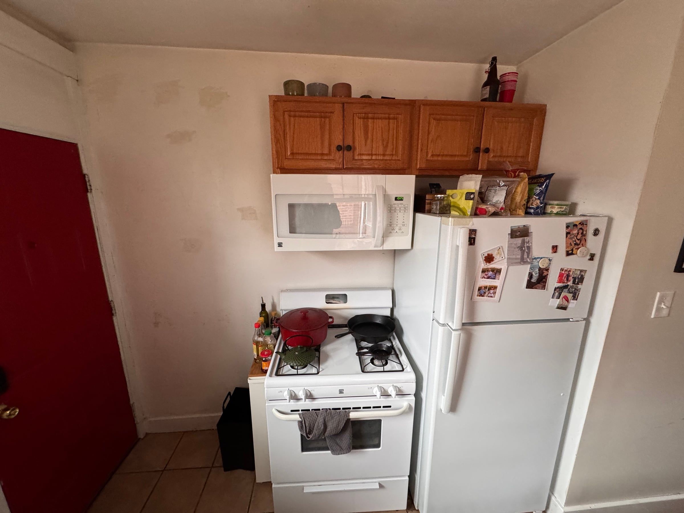 The kitchen before: a white range, microwave, and refrigerator under a short run of honey oak cabinets