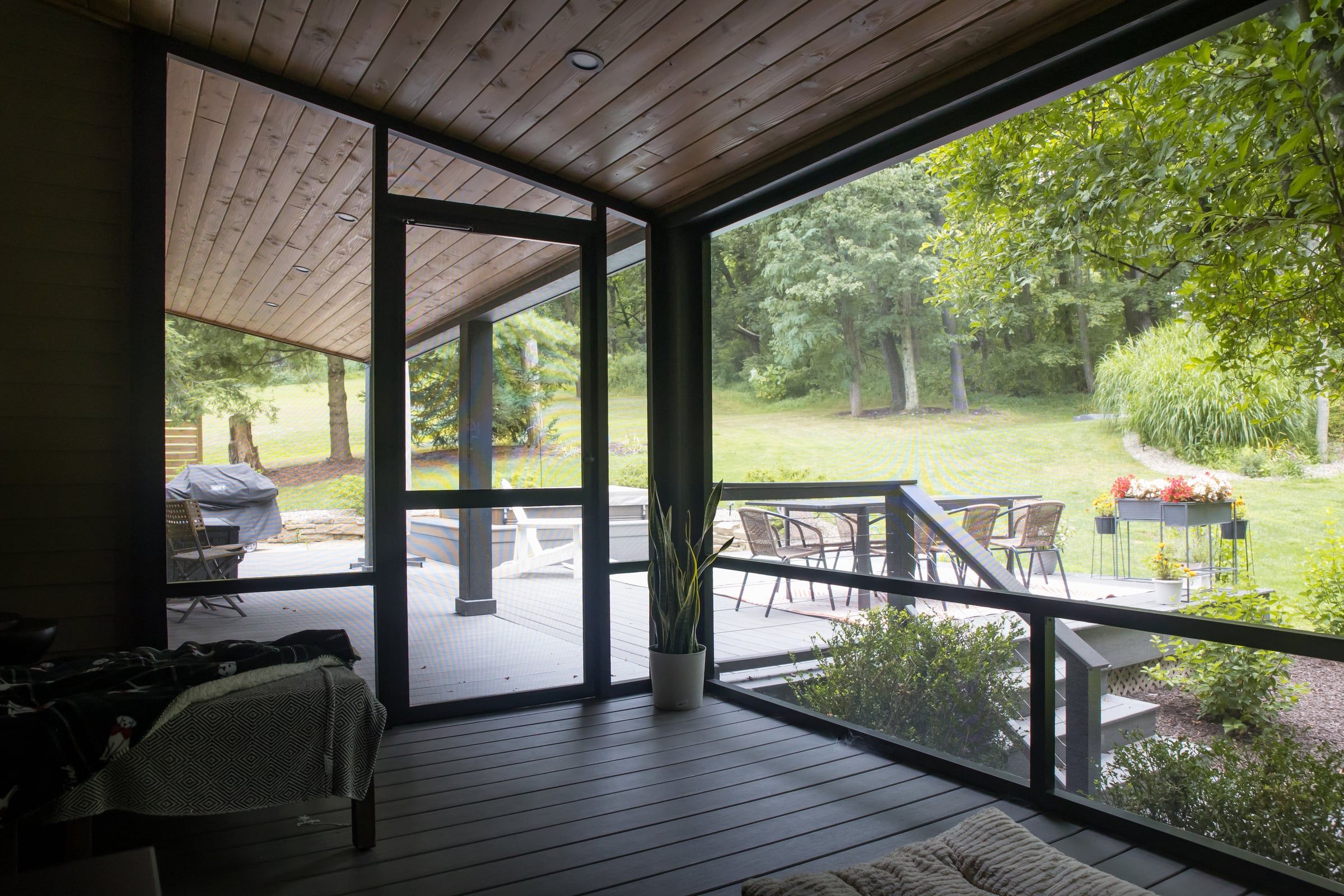 Inside the screen room: a cedar ceiling, black-framed screens, and wide views of the deck and the trees