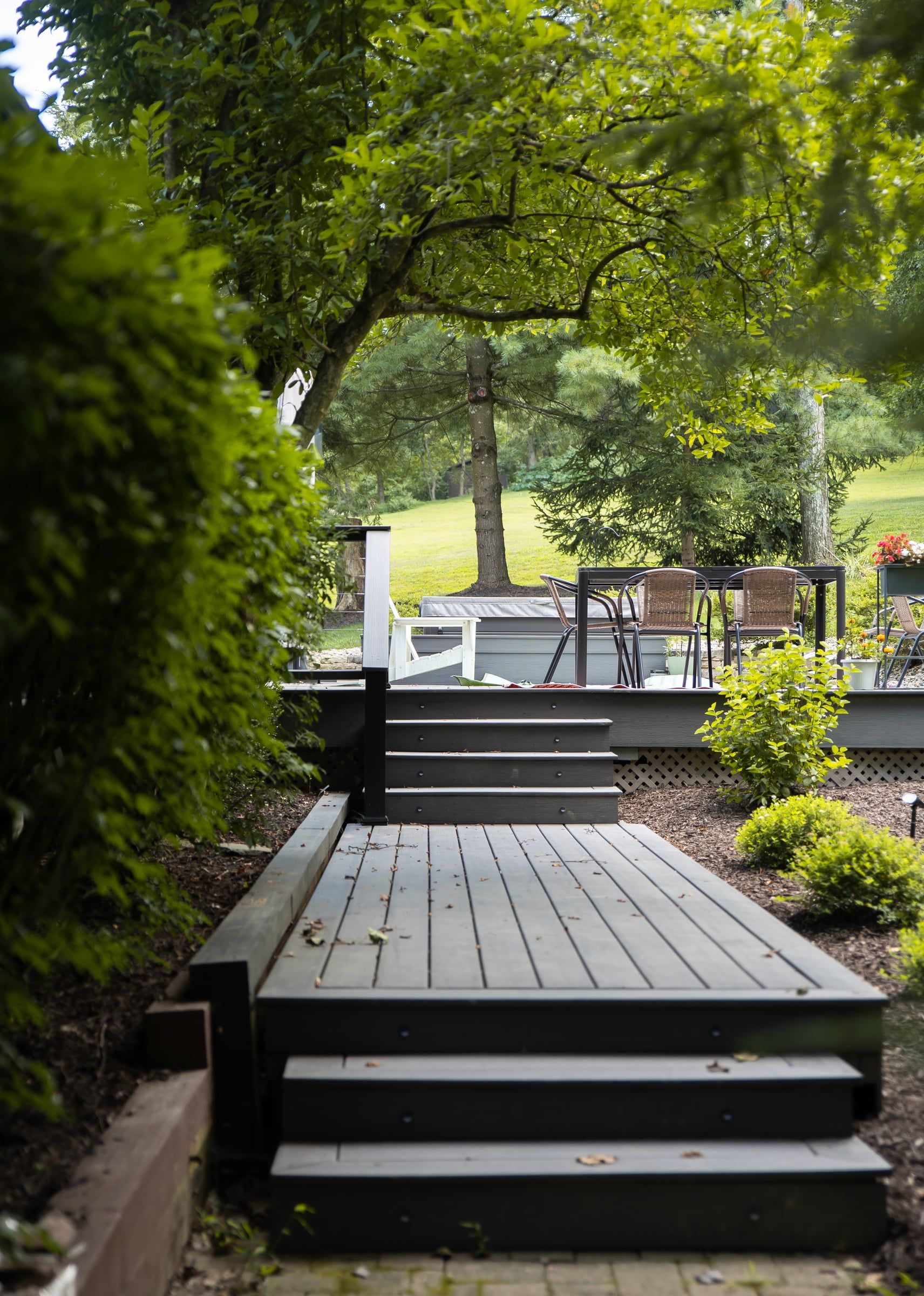 Dark composite deck stairs climbing through the garden to the upper deck, under the trees