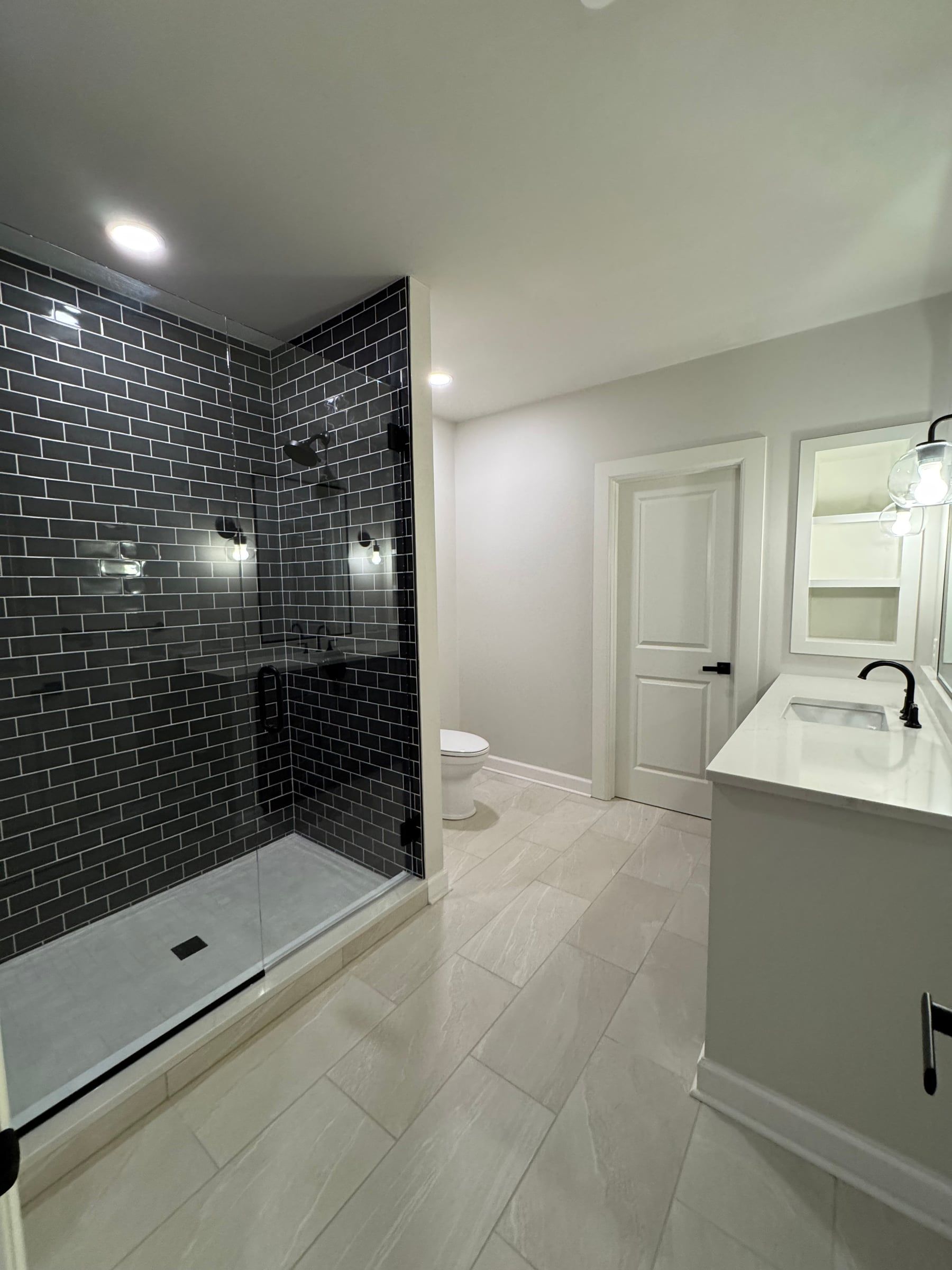 The full bathroom: a walk-in shower in dark subway tile, light floor tile, and a white vanity