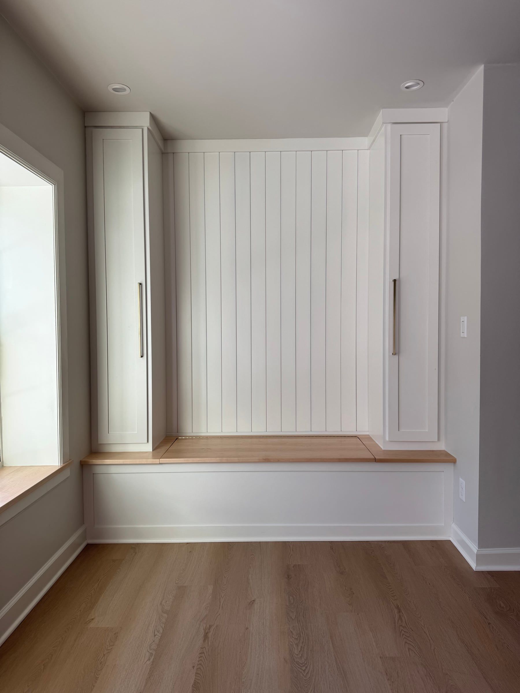 A built-in bench between two tall cabinets, with a paneled back, beside the back doors