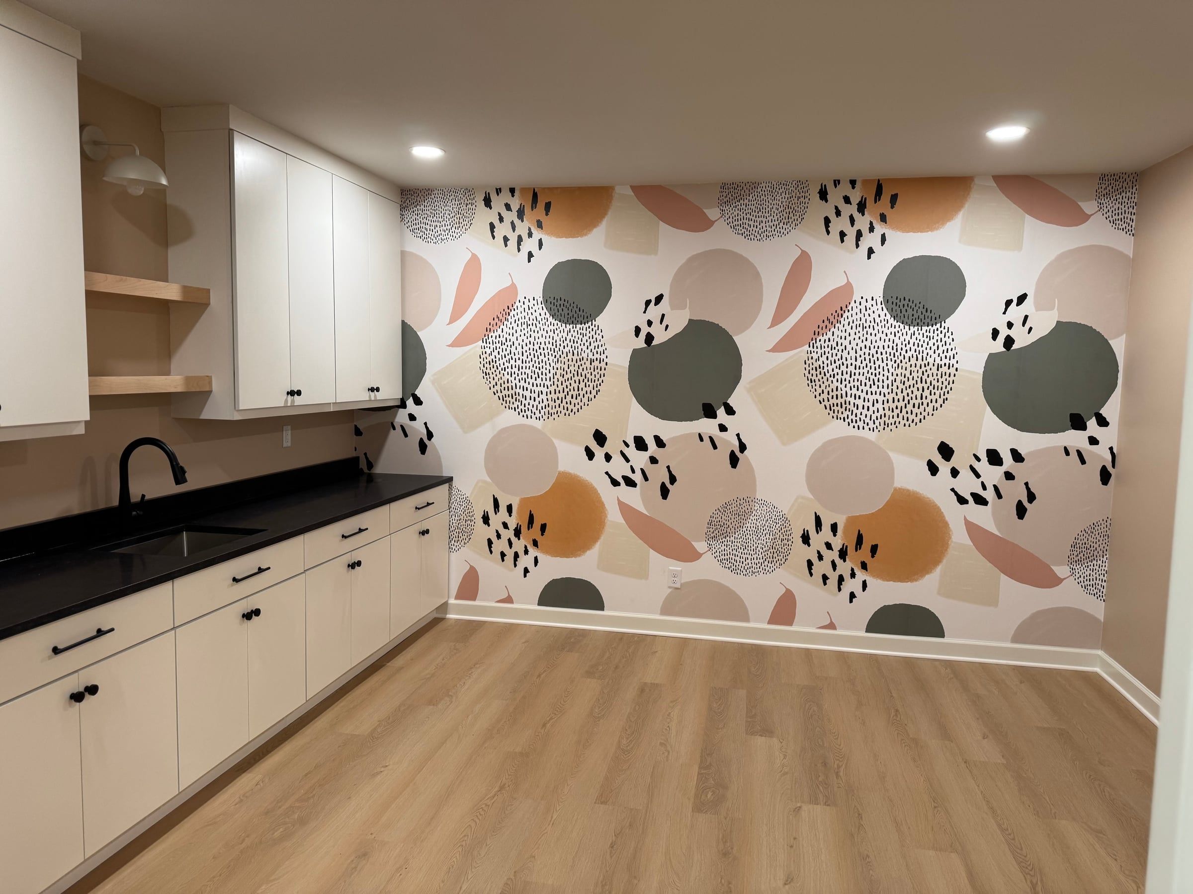 The craft room: white cabinets with a black counter and a utility sink, open shelves, and a wall of bold patterned wallpaper